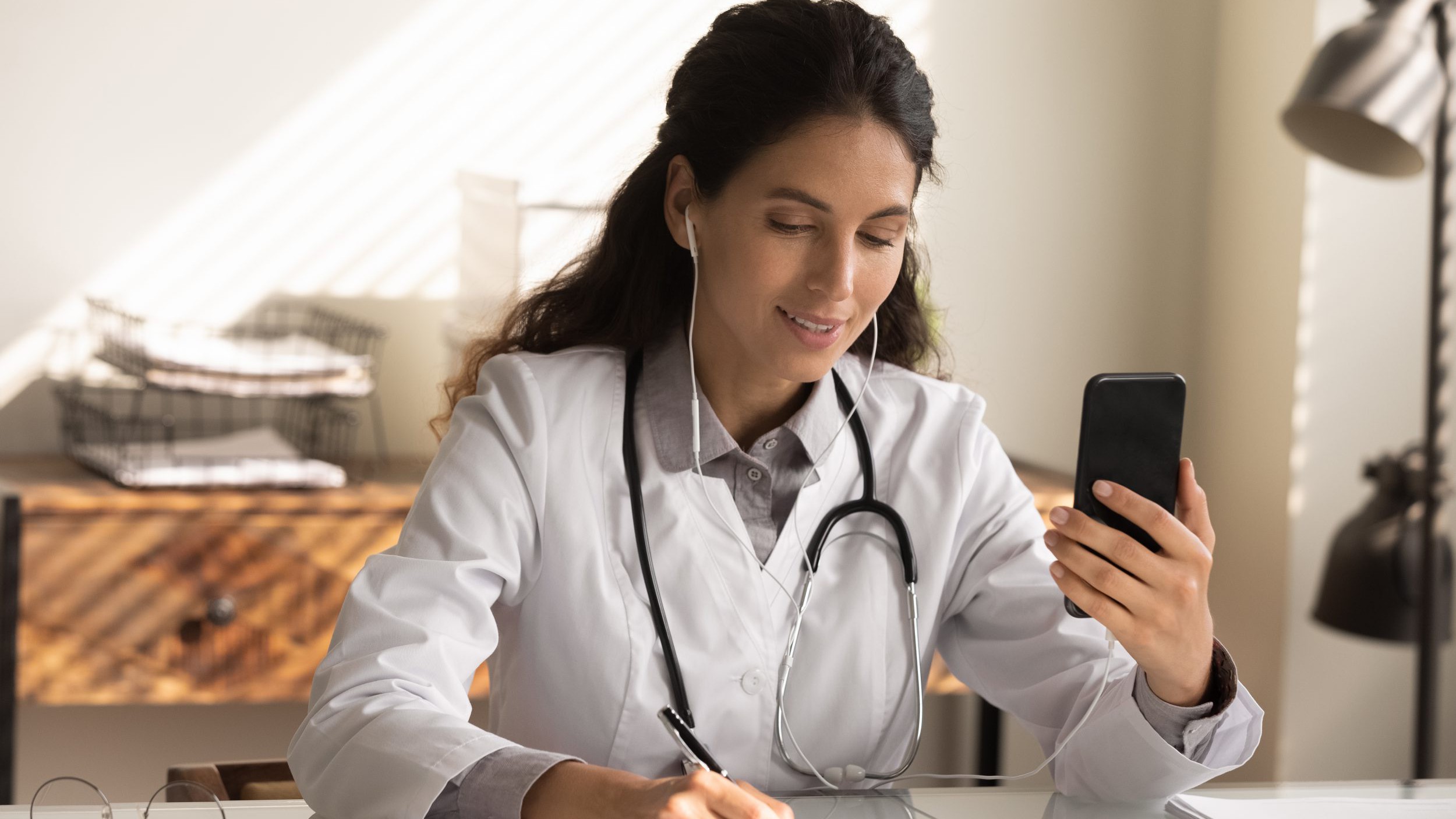 Close up female doctor wearing earphones holding phone, consulting online
