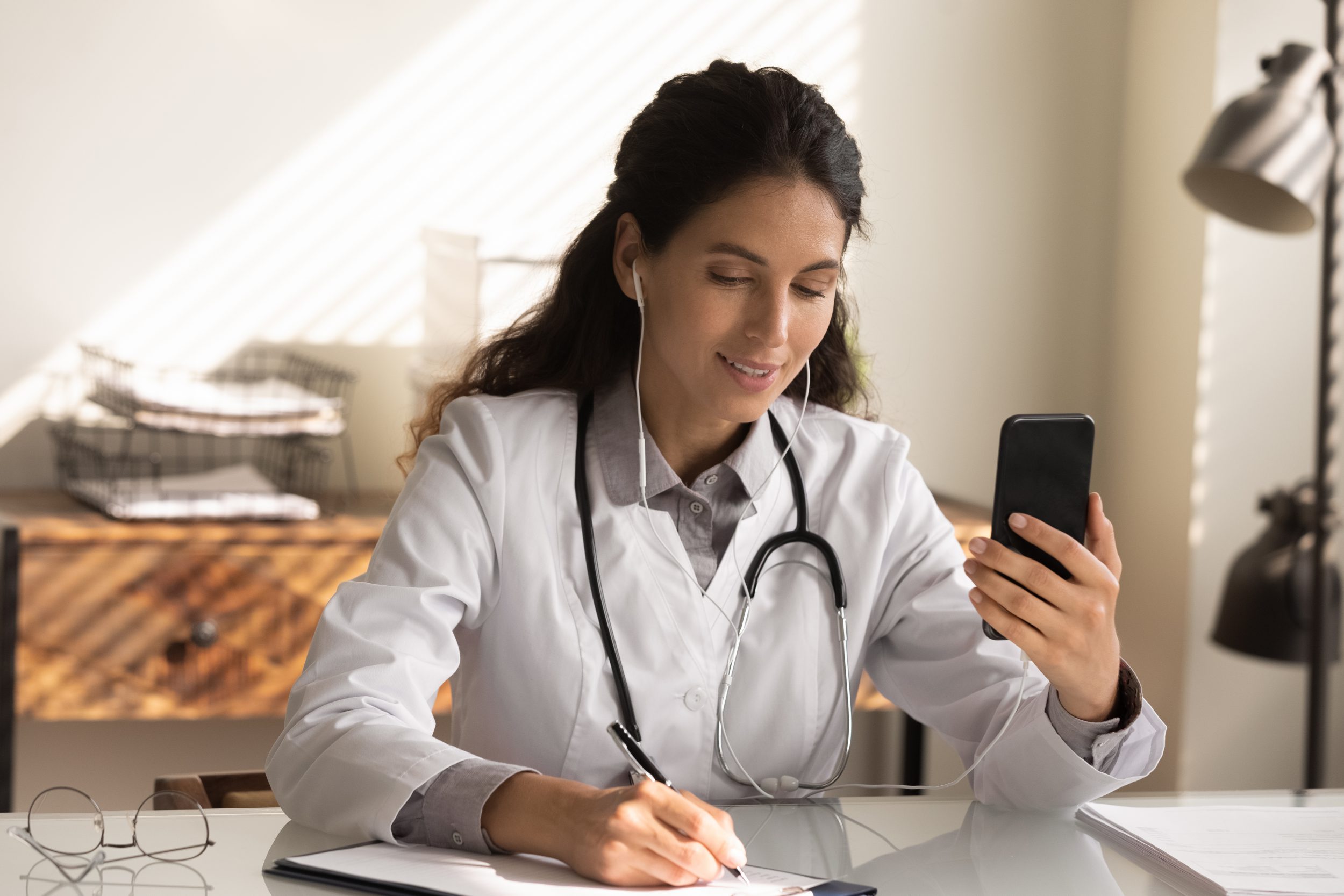 Close up female doctor wearing earphones holding phone, consulting online