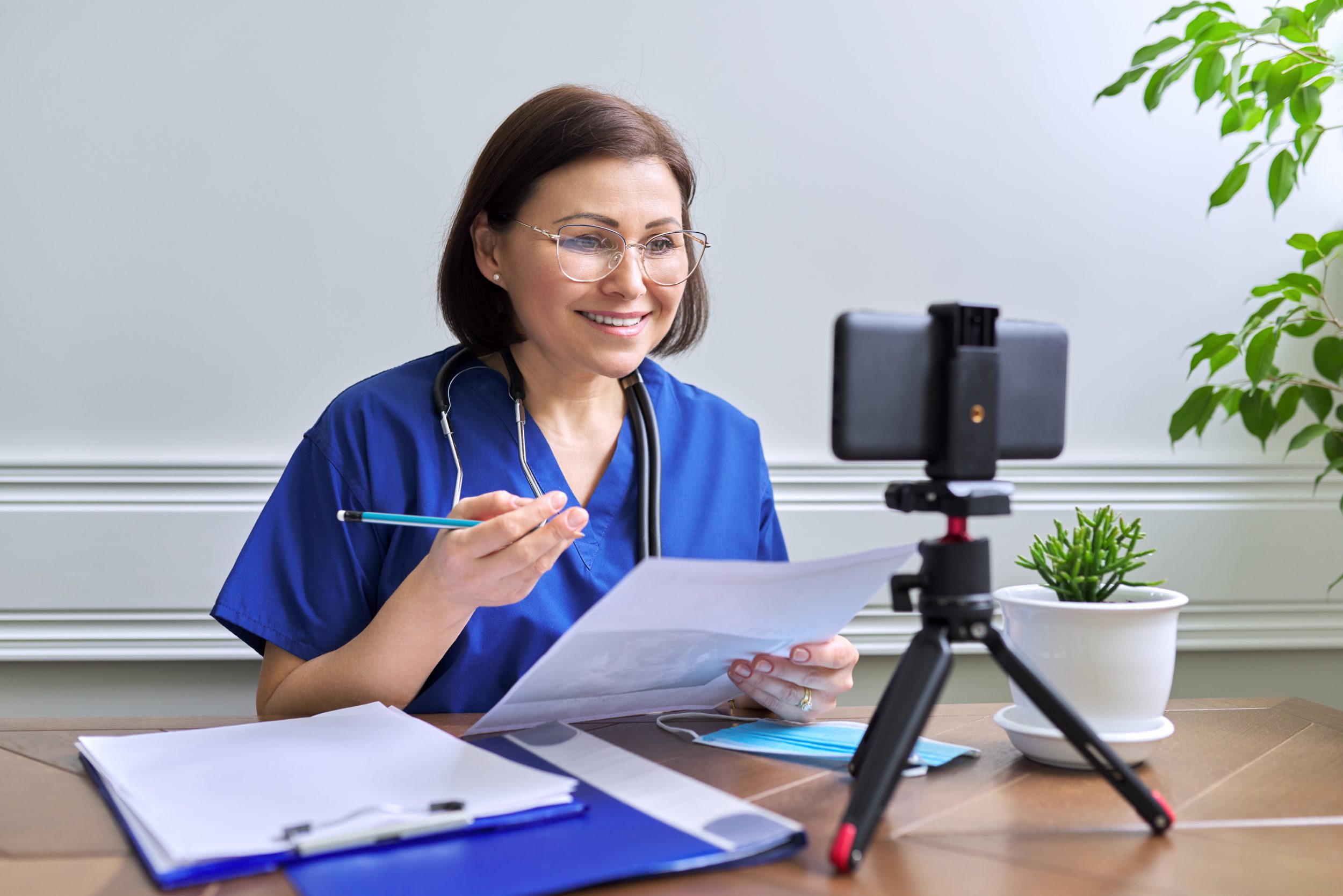 Online doctor consultation, female specialist talking with patient using video call, smartphone on tripod, doctor with stethoscope looking at the phone's webcam. Virtual patient sitting