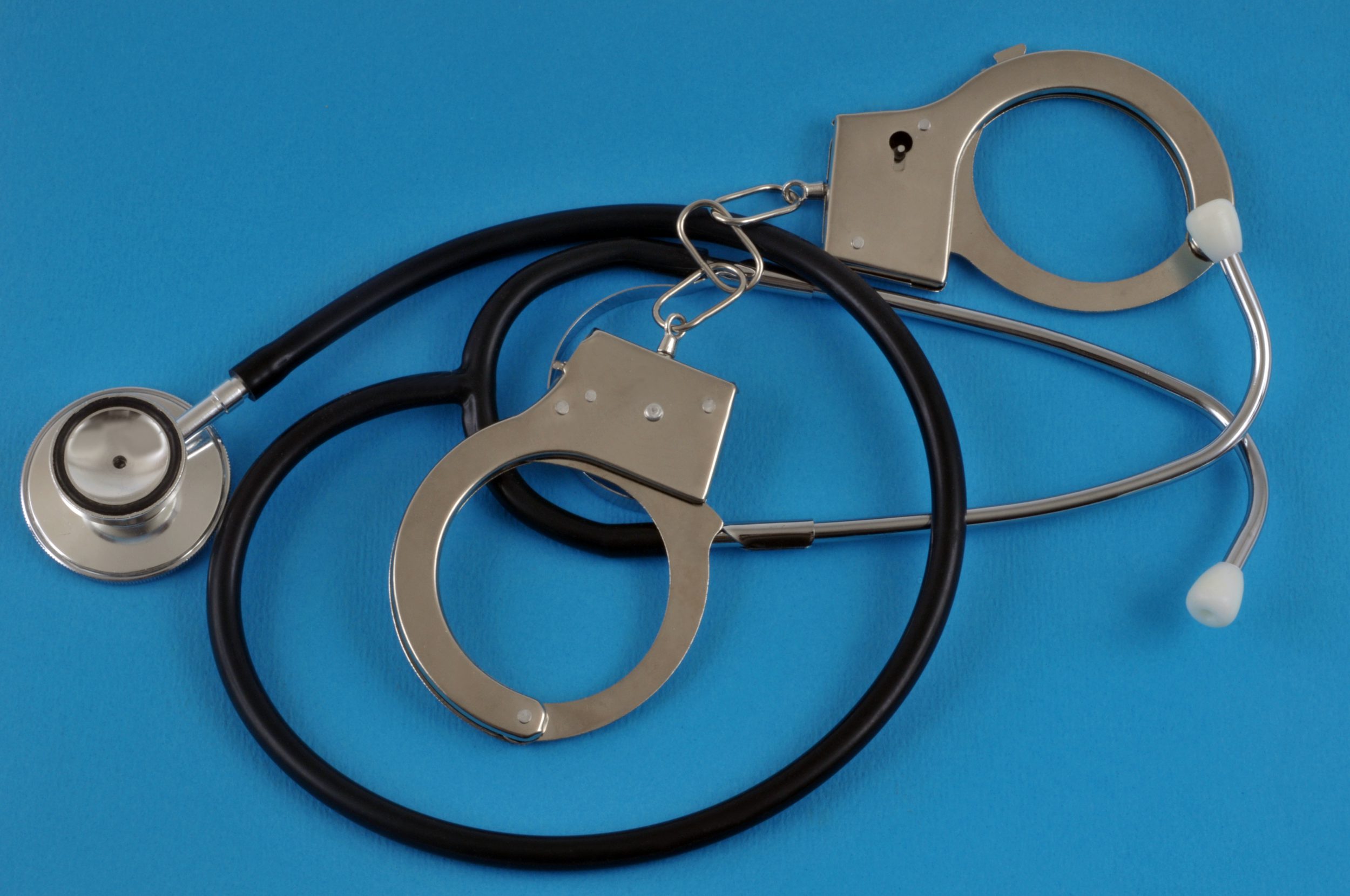 Medical error misdiagnosis concept with handcuffs and stethoscope on a blue background