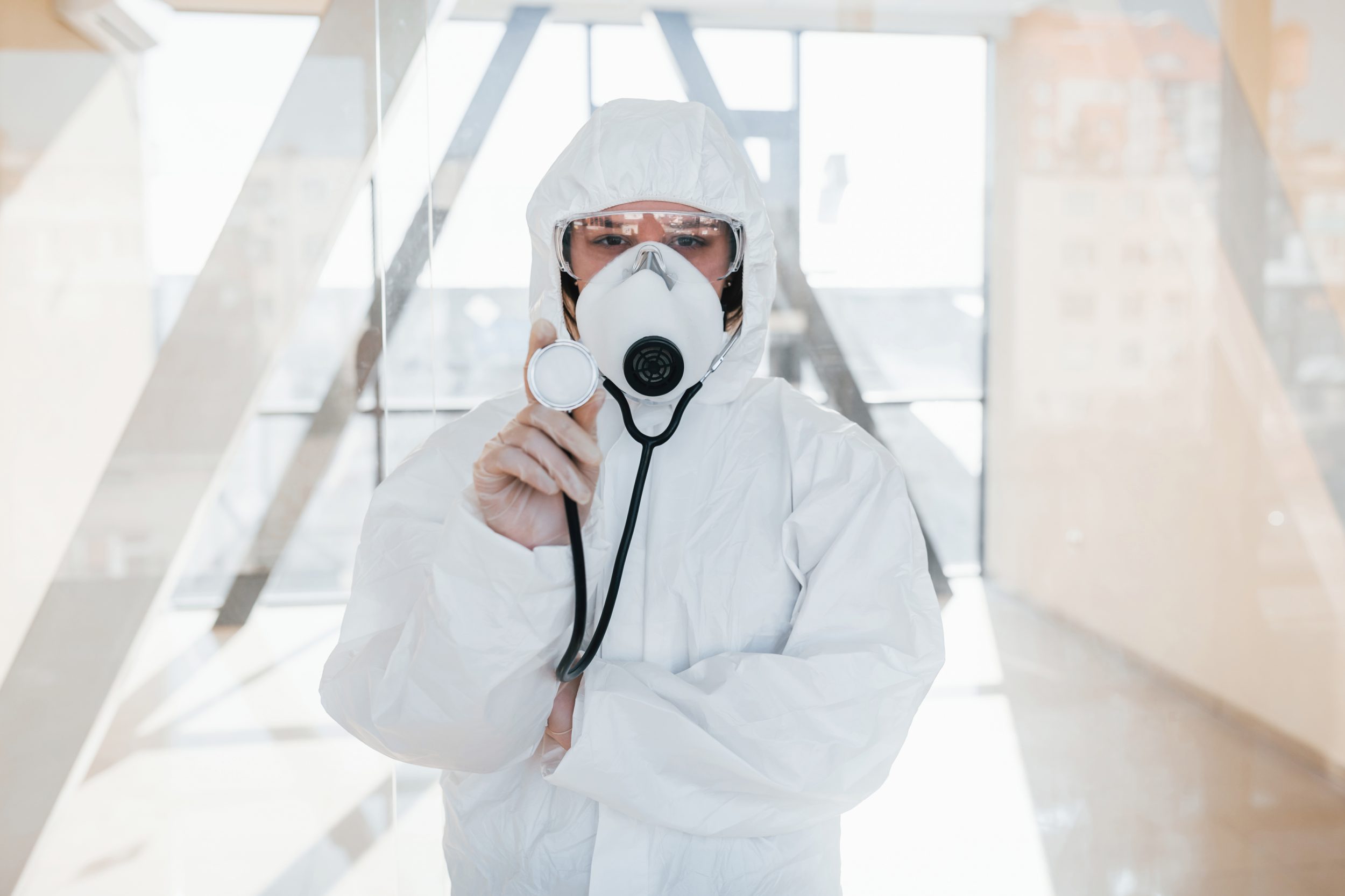 Female doctor scientist in lab coat, defensive eyewear and mask standing indoors and holds stethoscope to protect against Hospital waste greenhouse gas emissions