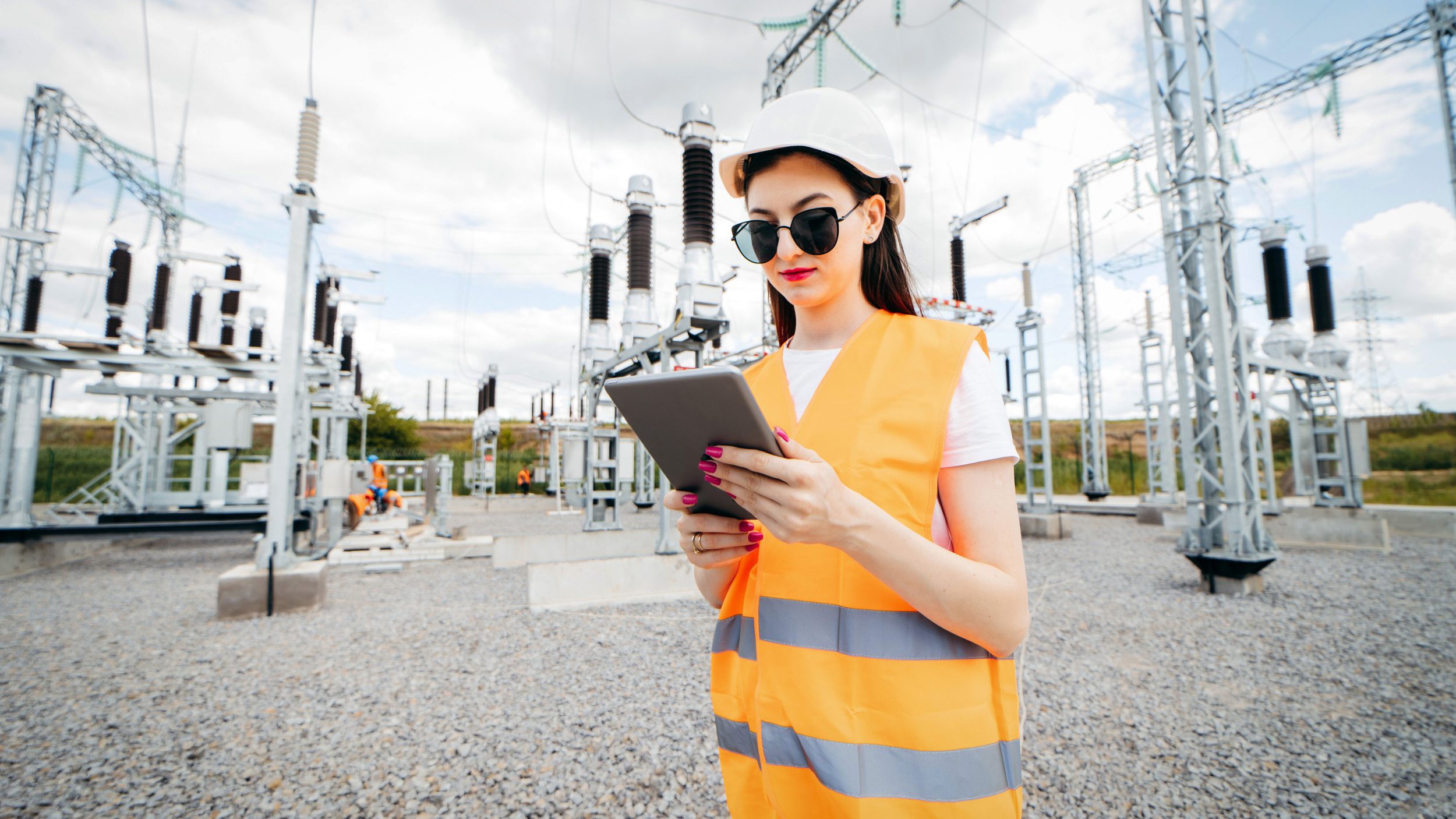 Adult woman energy engineer inspects the equipment of the smart grid modern power station using data from the tablet.