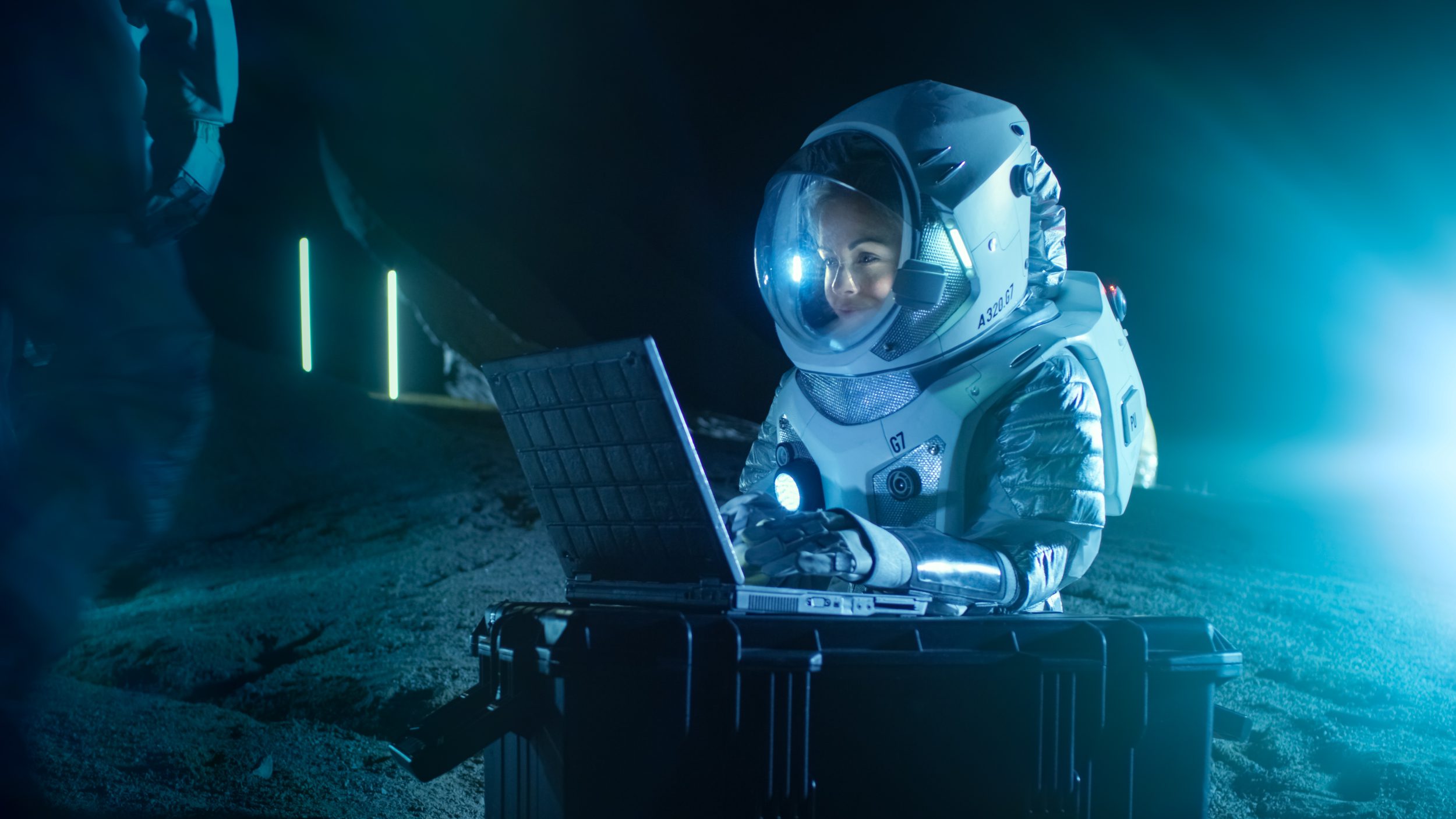 Computers in Space with Female Astronaut Wearing Space Suit Works on a Laptop, Exploring Newly Discovered Planet, Communicating with the Earth. In the Background Her Crew Member and Space Habitat.
