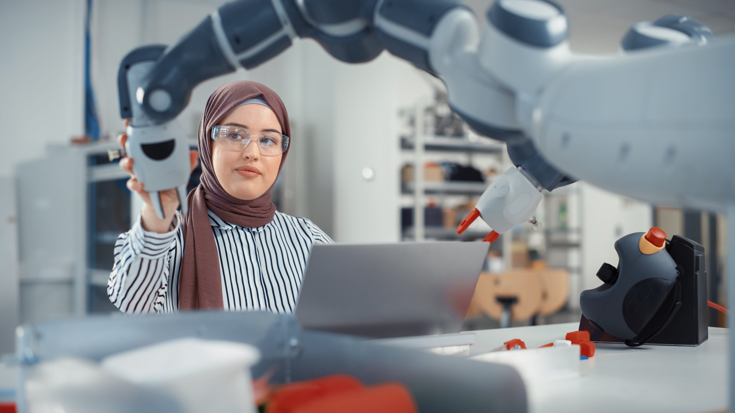 Muslim Businesswoman Wearing Hijab and Working on Engineering Project, Coding on Laptop and Changing industrial computer Robot Hand Position.